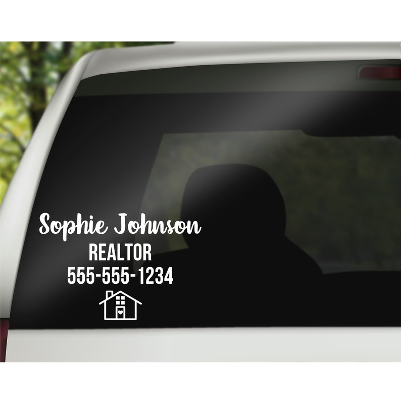 K&ouml;nnte beinhalten: Wei&szlig;er Autoaufkleber aus Vinyl mit dem Namen "Sophie Johnson", dem Titel "REALTOR", einer Telefonnummer und einem Haussymbol. Der Aufkleber befindet sich auf der Heckscheibe eines wei&szlig;en Fahrzeugs mit verschwommenem gr&uuml;nem Hintergrund.