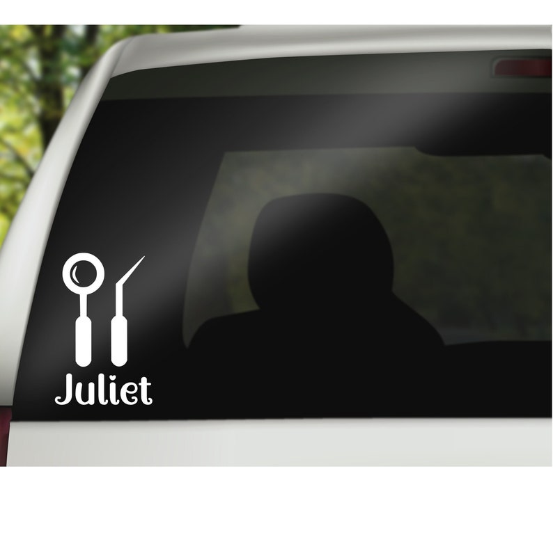 May include: A white dental tools sticker on a black car window. The tools include a mirror and a dental pick. The sticker also includes the word 'Juliet'.