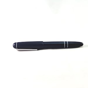 May include: A dark navy blue fountain pen with a smooth, matte finish. The pen features a silver-colored metal clip attached to the cap and two thin, parallel white horizontal lines encircling the barrel near the center of the writing instrument.