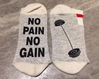 May include: A pair of grey and white socks with a red stripe. One sock has the text "NO PAIN NO GAIN" printed on it. The other sock has a black and white illustration of a barbell.