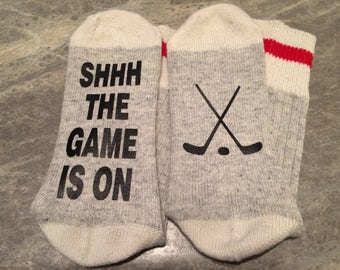 Shhh The Game Is On .... (Hockey Sticks and Puck Silhouette) (Word Socks - Funny Socks - Novelty Socks)