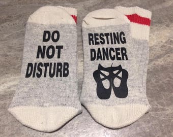 May include: A pair of grey and white socks with red stripes. One sock says "Do Not Disturb" and the other says "Resting Dancer" with a graphic of two ballet shoes.
