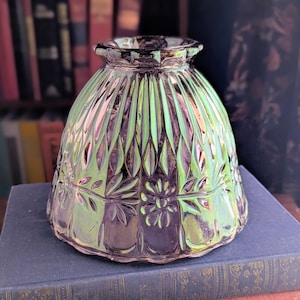 May include: A bell-shaped glass lamp shade featuring an iridescent purple finish with a reflective sheen. The surface is decorated with a molded pattern of vertical fluting, embossed floral motifs, and leaves encircling the lower section.
