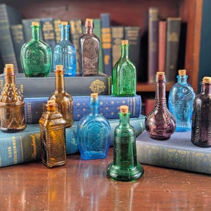 May include: An assortment of vintage glass bottles in shades of green, blue, amber, and purple, each with a cork. The bottles are displayed on a wooden surface and on top of old books, creating a vintage aesthetic.