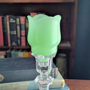 Peut inclure: Un abat-jour de bougeoir en verre vert clair en forme de fleur de tulipe, doté de pétales en verre opaque, lisse et pastel. L'abat-jour est conçu pour être placé sur une base de bougeoir en verre transparent à facettes avec une tige géométrique.