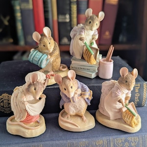 May include: A collection of five anthropomorphic mouse figurines in various poses. One mouse holds a blue rice barrel, another sweeps with a broom on books, one adjusts a white apron, one wears a blue jacket, and one sweeps with a broom.