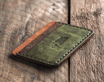 Puede incluir: Un porta tarjetas de cuero verde con un acento de cuero marrón y la palabra "LUVA" grabada en la parte delantera.