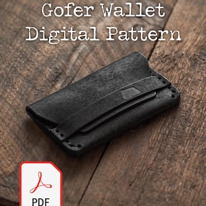 Puede incluir: Cartera de cuero negro con cierre de correa, sobre un fondo de madera rústica. El texto "Gofer Wallet Digital Pattern" se muestra encima de la cartera. Un icono PDF está en la esquina inferior izquierda.