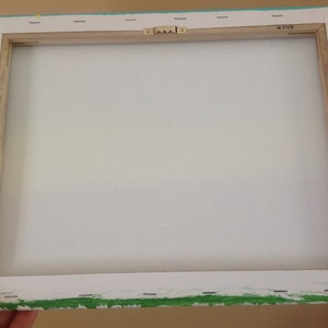 May include: The back of a stretched canvas painting with a wooden frame. The canvas is white and the frame is painted turquoise with green accents. The frame has a metal hanging hook.