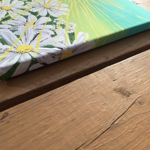May include: A close-up of a canvas painting with a white daisy design. The background is a gradient of yellow, green, and blue. The painting is signed "Joy Russell" in the bottom left corner.