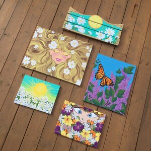May include: Five paintings on canvas with floral and nature themes. One painting features a woman with blonde hair and white flowers, another has a butterfly on a purple flower, and another has a sun with white flowers. The remaining two paintings feature a woman's face with flowers.