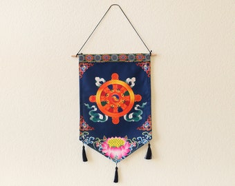 Könnte beinhalten: Ein blauer Wandteppich mit einem farbenfrohen Dharma-Rad-Design und einer rosa Lotusblume am unteren Rand. Der Wandteppich hängt an einer weißen Wand über einem weißen gekachelten Kamin.