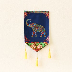 May include: A blue and colorful tapestry with an elephant design and yellow tassels hanging from the bottom.