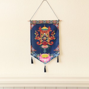 May include: A blue tapestry with a colorful mandala design featuring a wheel of life, lotus flowers, and intricate patterns. The tapestry is hanging from a wooden dowel and has tassels on the bottom.