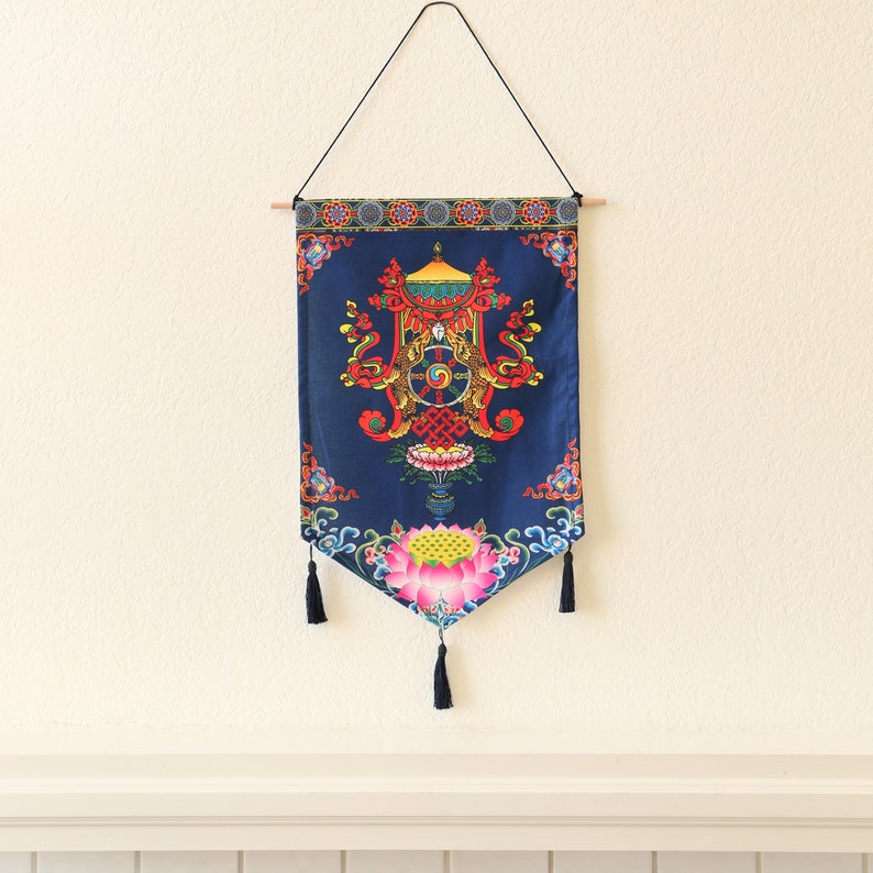 May include: A blue tapestry with a colorful mandala design featuring a wheel of life, lotus flowers, and intricate patterns. The tapestry is hanging from a wooden dowel and has tassels on the bottom.