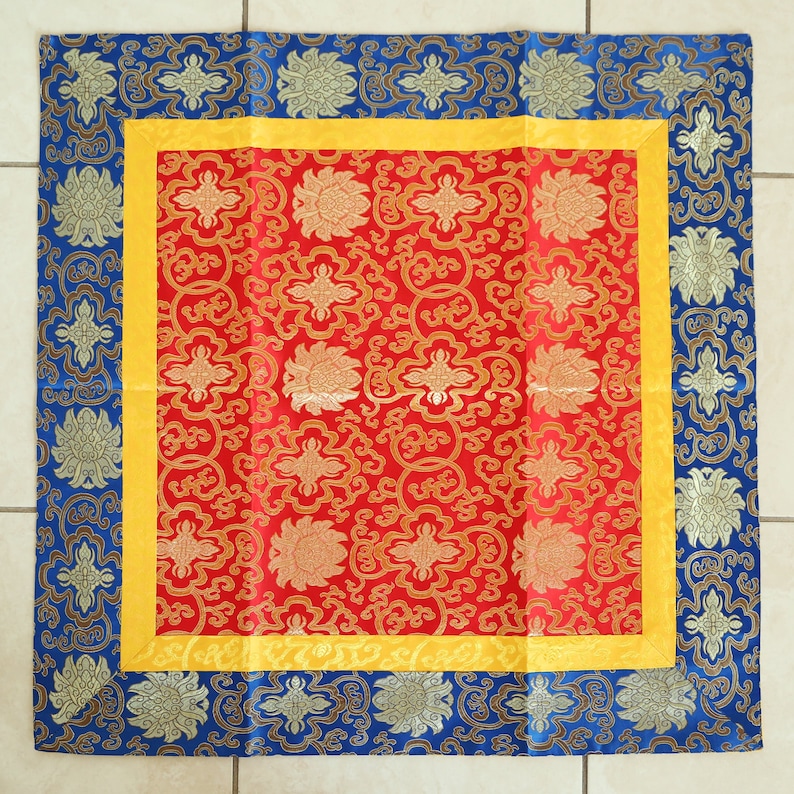 Puede incluir: Un coj&iacute;n cuadrado con un dise&ntilde;o floral rojo, amarillo y azul. El coj&iacute;n tiene un borde decorativo.