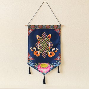 May include: A blue tapestry with a colorful knot design and a lotus flower at the bottom. The tapestry is hanging from a wooden dowel rod.