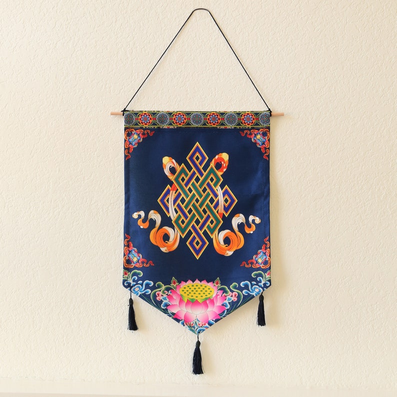 May include: A blue tapestry with a colorful knot design and a lotus flower at the bottom. The tapestry is hanging from a wooden dowel rod.