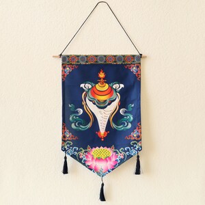 May include: A blue tapestry with a white conch shell design and a lotus flower at the bottom. The tapestry has a fringe border and is hanging from a wooden dowel.