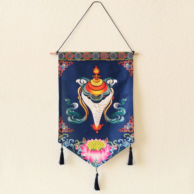 May include: A blue tapestry with a white conch shell design and a lotus flower at the bottom. The tapestry has a fringe border and is hanging from a wooden dowel.