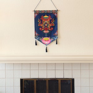 May include: A blue tapestry with a colorful mandala design hangs above a white tiled fireplace with a black metal screen.