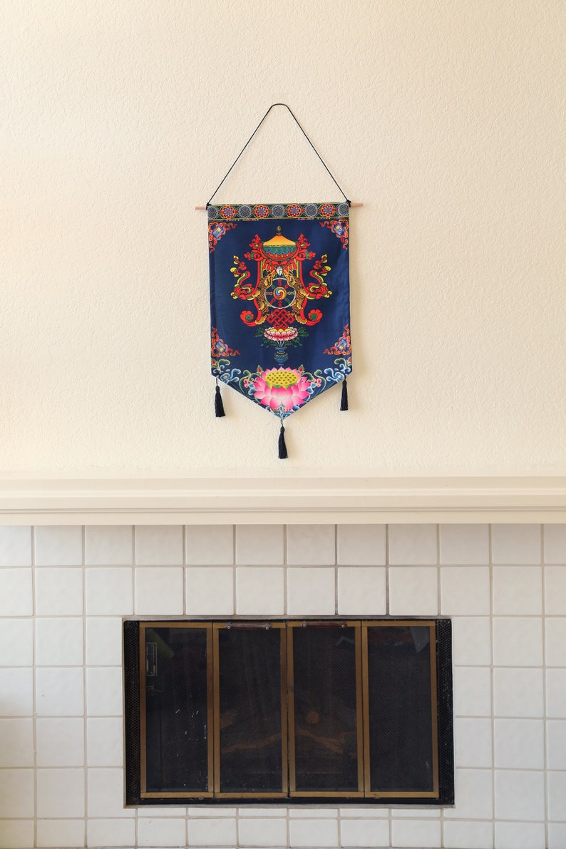 May include: A blue tapestry with a colorful mandala design hangs above a white tiled fireplace with a black metal screen.