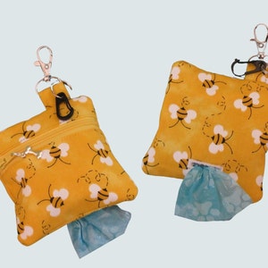 May include: Two yellow fabric bags with a bee pattern and a zipper closure. Each bag has a silver clip and a black clip attached to the top. The bags are filled with blue plastic bags.