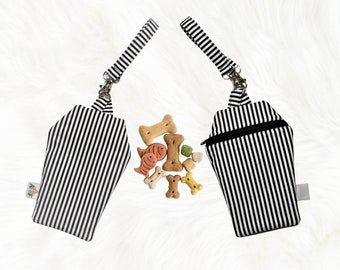 May include: Two black and white striped treat pouches with a zipper closure and a black strap. The pouches are shaped like a coffin and are filled with dog treats.