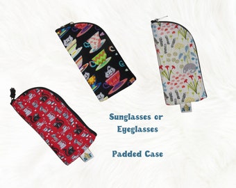 May include: Three different patterned padded cases for sunglasses or eyeglasses. The cases are black with a teacup and cat design, white with a floral and sloth design, and red with a cat design.