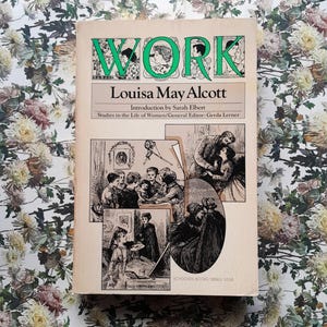 Puede incluir: Un libro de bolsillo vintage titulado "WORK" de Louisa May Alcott. La portada presenta ilustraciones y texto en verde y negro, con el título en un lugar destacado. El libro está sobre un fondo con estampado floral.
