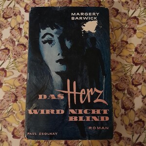 May include: A vintage book titled "Das Herz Wird Nicht Blind" by Margery Barwick. The cover features a woman's face and a silhouette, with text in pink and white against a dark blue background. The book is a Roman.