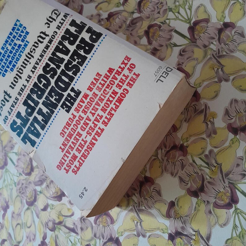 May include: A paperback book titled "Presidential Transcripts" with the text "The Complete Transcripts of the Nixon Tapes." The cover is white with blue and black text. The book is slightly angled, revealing its aged edges.