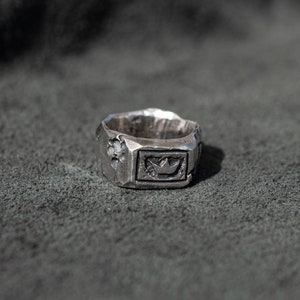 May include: A silver ring with a textured surface and a crown design in the center.