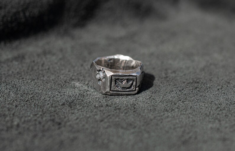 May include: A silver ring with a textured surface and a crown design in the center.