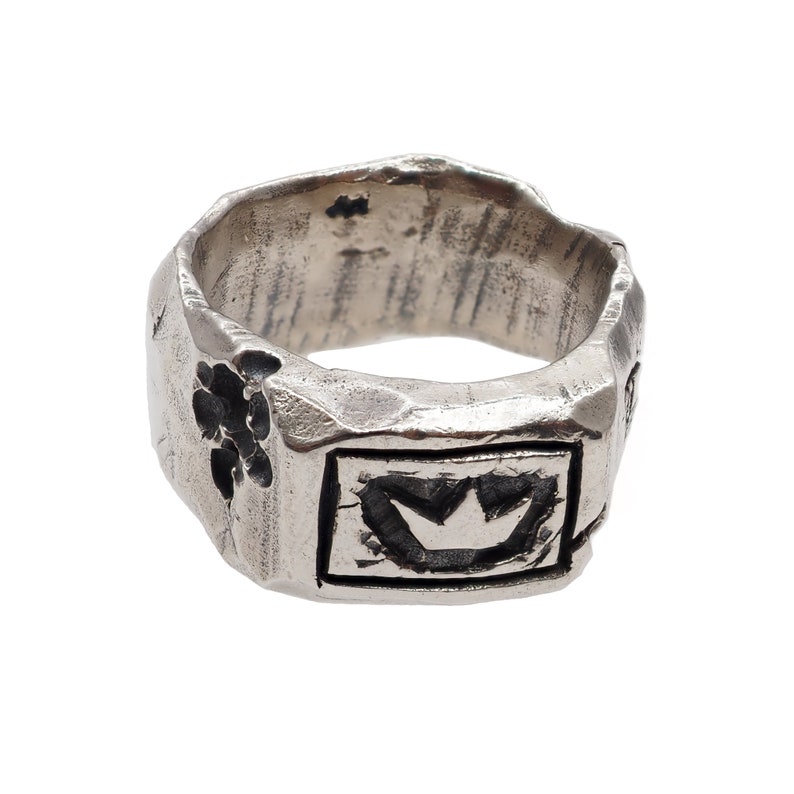 May include: A silver ring with a textured surface and a crown design. The ring has a floral design on one side.