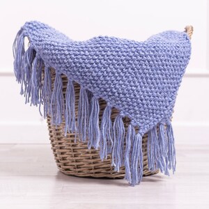 May include: A light blue knitted throw blanket with fringe, folded and placed in a wicker basket.