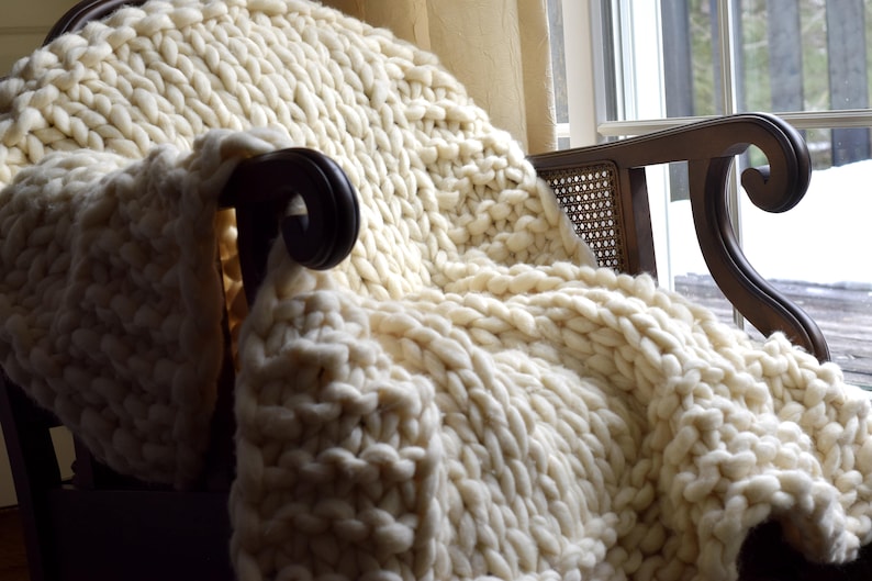 May include: A white chunky knit throw blanket draped over a wooden armchair with a woven cane back.