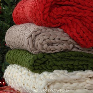 Puede incluir: Una pila de cuatro mantas de punto grueso en rojo, beige, verde y blanco. Las mantas est&aacute;n dobladas y apiladas una encima de la otra. Las mantas est&aacute;n hechas de hilo grueso y tienen una textura suave y acogedora.