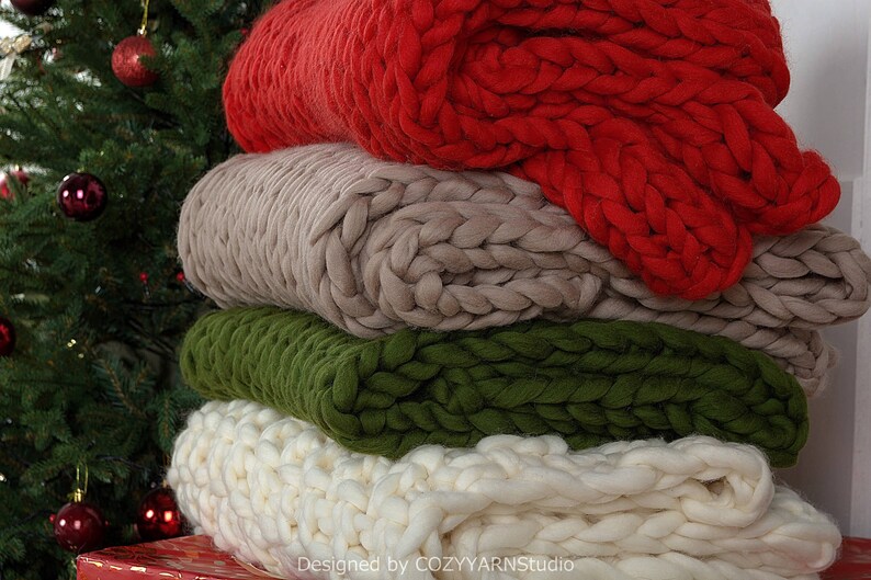 Puede incluir: Una pila de cuatro mantas de punto grueso en rojo, beige, verde y blanco. Las mantas est&aacute;n dobladas y apiladas una encima de la otra. Las mantas est&aacute;n hechas de hilo grueso y tienen una textura suave y acogedora.