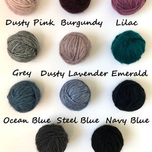 May include: Balls of yarn in various colors, including dusty pink, burgundy, lilac, grey, dusty lavender, emerald, ocean blue, steel blue, navy blue, dark grey, and black.