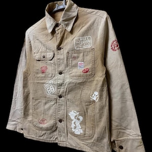 May include: A tan work jacket with multiple patches, including a "Wile E. Coyote Genius" patch, a "Route 66" patch, and a cartoon character patch.