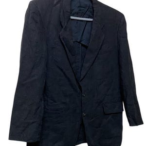 May include: A black blazer hanging on a gray hanger. The blazer has a two-button closure, a notched lapel, and a single chest pocket. The fabric appears to be a textured weave. The blazer is a classic style.