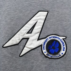 Puede incluir: Sudadera gris con una aplicaci&oacute;n de fieltro blanco de una letra A grande y un parche circular con el texto "University of North Carolina Asheville" y una huella de pata azul.