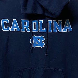 May include: A navy blue hooded sweatshirt with the word "CAROLINA" in white lettering with blue outlines and a blue and white "NC" logo.