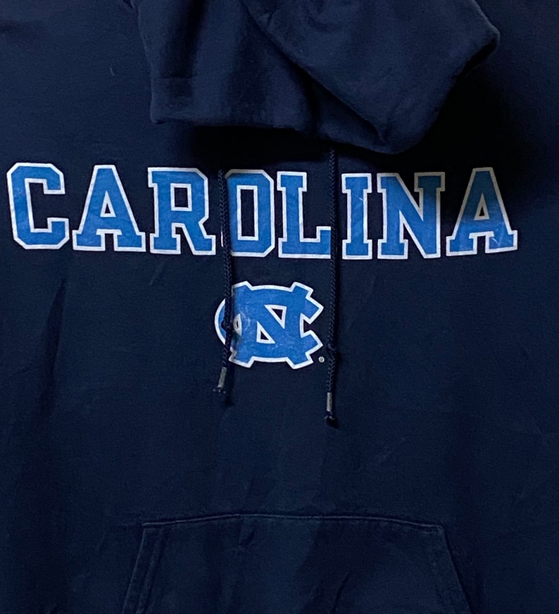 May include: A navy blue hooded sweatshirt with the word "CAROLINA" in white lettering with blue outlines and a blue and white "NC" logo.