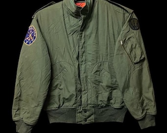 May include: Olive green bomber jacket with a ribbed collar, cuffs, and hem. Features a zip closure, multiple pockets, and patches on the sleeves. The jacket has a military-inspired design and a quilted lining.