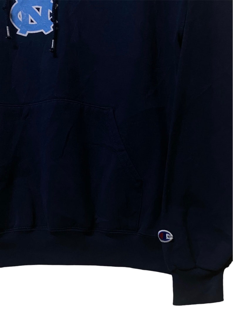 May include: A navy blue hooded sweatshirt with a blue and white North Carolina Tar Heels logo on the front and a Champion logo on the left sleeve.