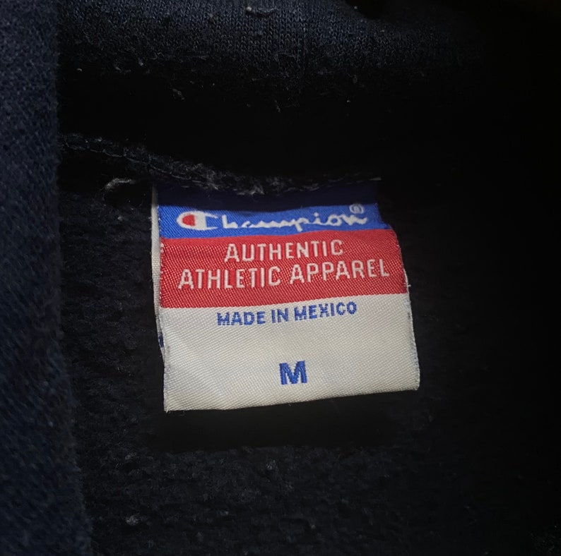 May include: A white tag with black text that reads "Champion Authentic Athletic Apparel Made in Mexico" and a size "M" in black text.