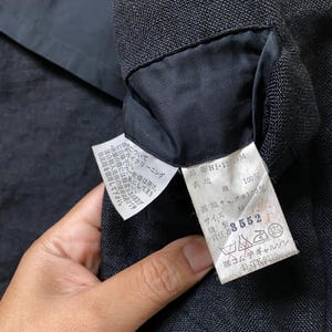 May include: Close-up of a black garment's interior, revealing a sewn-in label. The label displays Japanese text, fabric composition, and care instructions. The garment's texture is visible, with a focus on the label's details.