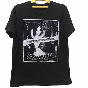 May include: Black t-shirt with a graphic print. The print features a black and white image of a woman inside a decorative frame, with the text "I RESERVE THE RIGHT TO REFUSE SERVICE TO ANYONE."